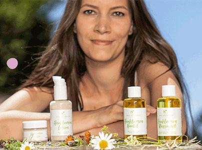 Frau mit Heu-Naturkosmetik-Produkten auf einem Tisch, umgeben von Kräutern und Blüten in der Natur