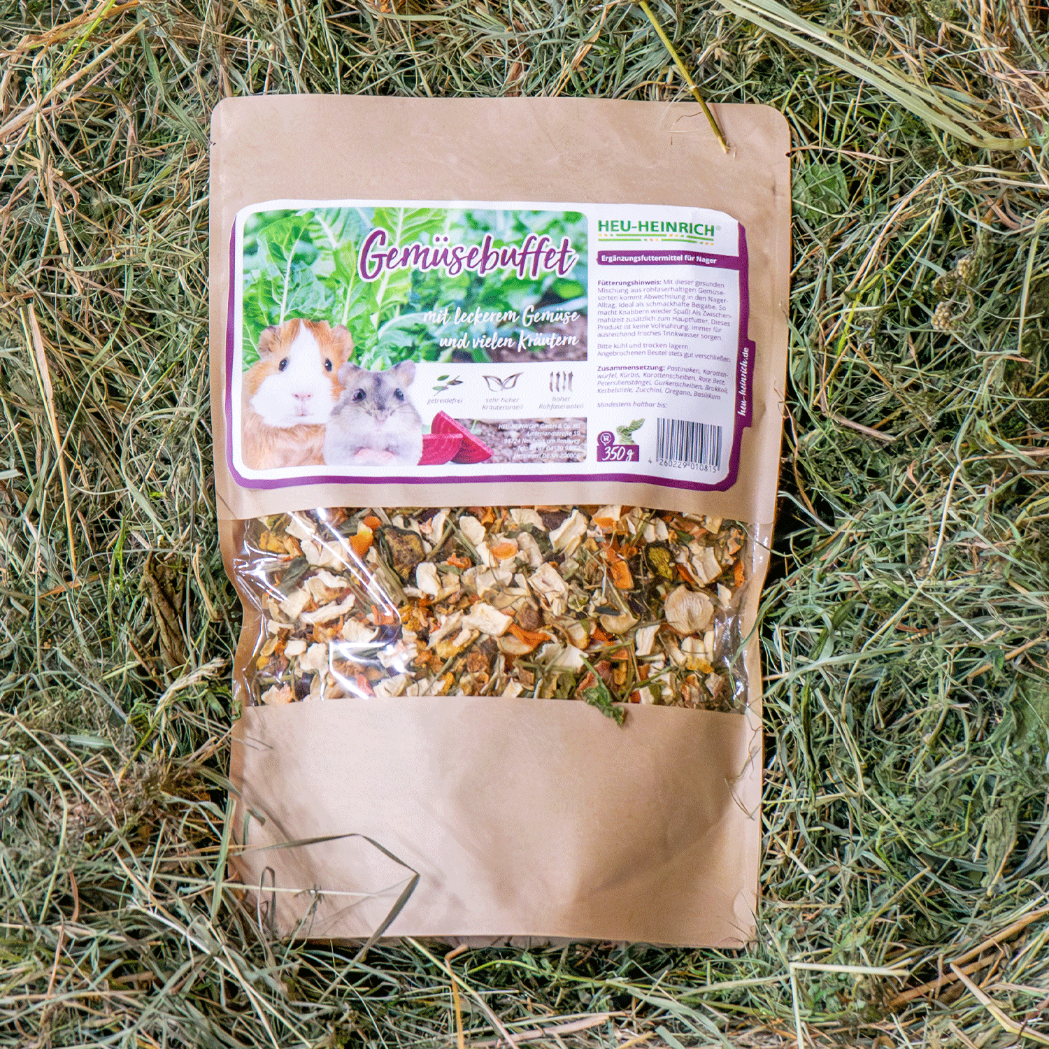 350g Futtermischung "Gemüsebuffet" von Heu-Heinrich, Trockenfutter für Nager. Ergänzungsfuttermittel Foto von der braunen Papierverpackung mit Foliensichtfenster. Auf Heu liegend.