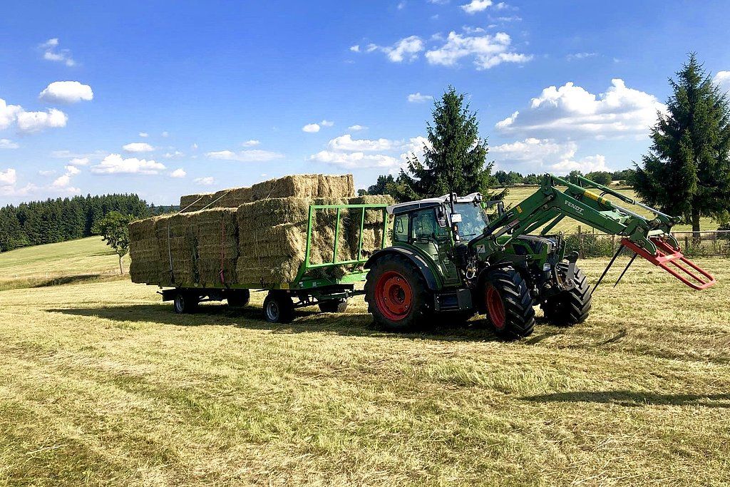 Traktor mit Heuballen-Anhänger auf Wiese im Thüringer Wald bei der Ernte von Bergwiesenheu